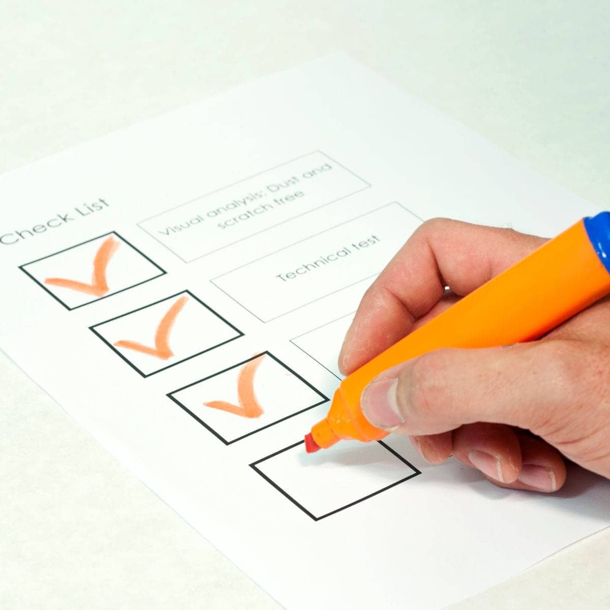 Surligneur orange avec un capuchon bleu utilisé pour marquer des cases cochées sur une liste de contrôle.